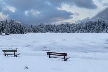 Germany, Bavaria, Berchtesgaden, Berchtesgadener Alps,  Snow covered and frozen Lake Hintersee with seats by the lakeside.