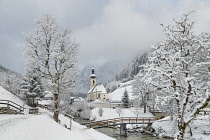 Germany, Bavaria, Ramsau village, famous vista of the Church of  St Sebastian with the footbridge over the Ramsauer Ache river in a snow covered landscape.