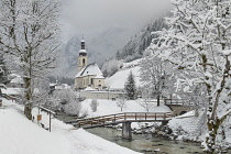 Germany, Bavaria, Ramsau village, famous vista of the Church of  St Sebastian with the footbridge over the Ramsauer Ache river in a snow covered landscape.