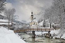 Germany, Bavaria, Ramsau village, famous vista of the Church of  St Sebastian with the footbridge over the Ramsauer Ache river in a snow covered landscape.