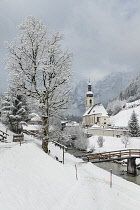 Germany, Bavaria, Ramsau village, famous vista of the Church of  St Sebastian with the footbridge over the Ramsauer Ache river in a snow covered landscape.