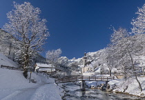 Germany, Bavaria, Ramsau village, famous vista of the Church of  St Sebastian with the footbridge over the Ramsauer Ache river in a snow covered landscape.