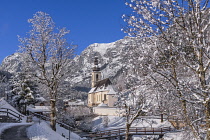 Germany, Bavaria, Ramsau village, famous vista of the Church of  St Sebastian with the footbridge over the Ramsauer Ache river in a snow covered landscape.