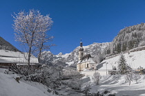 Germany, Bavaria, Ramsau village, famous vista of the Church of  St Sebastian with the Ramsauer Ache river in a snow covered landscape.