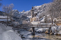 Germany, Bavaria, Ramsau village, famous vista of the Church of  St Sebastian with the footbridge over the Ramsauer Ache river in a snow covered landscape.