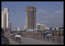 China, Guangdong, Shenzen, Cyclists and cars on road in front of skyscraper under construction.