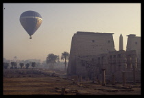 Egypt, Luxor, Tourist hot air balloon over ruined temple in early evening light.