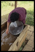 Brazil, Minas Gerais, Near Ouro Preto, Man panning for gold with large metal dish in muddy water trough.