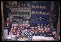 China, Xinjiang, Kashgar, Moslem caps for sale on stall with vendor.