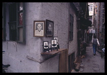 China, Guangdong, Guangzhou, Backstreet with shrine to ancestors on the corner and pedestrians walking past.