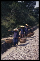 China, Guangxi, Three women on the road to market carrying baskets on poles over their shoulders.