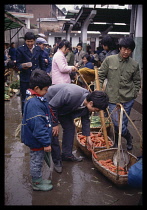 China, Hunan, Huaihua, Man and young boy buying carrots in a street market on a rainy day.