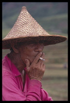 China, Hainan Island, People, Farmer in conical hat smoking a cigarette, head and shoulders three-quarter profile portrait.