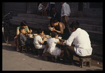 China, Henan Province, Kaifeng, Adults and children eating breakfast at street food stall on the way to work and school.