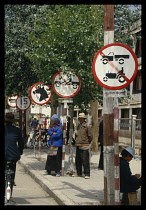 China, Tibet, Lhasa, Street signs lining the road with people waiting and a cyclist passing.