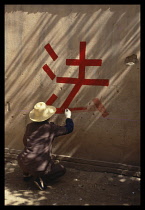 China, General, Man painting slogan in Chinese calligraphy onto a wall with red paint .