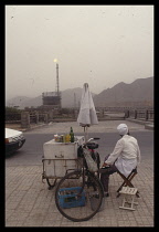 China, Gansu, Lanzhou, Drinks vendor outside oil refinery with burn off flame visible.
