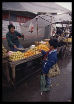 China, Hunan, Huaihua, Boy buying oranges from a market vendor.