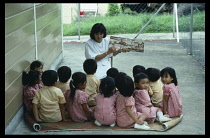 Malaysia, Kedah, Kuching, Anglican Mission.School girls sitting on a mat facing teacher holding a book.