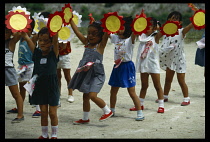 Japan, Honshu, Kyoto, School children standing in a line in the playground holding paper flowers in the air above their heads.