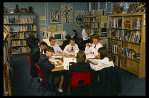 Education, Secondary School, Library, Male and female pupils studying at table in library  other pupils using computers behind.