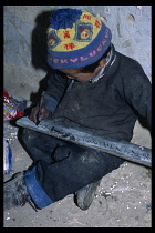 China, Tibet, Shigatse, Primary school child sitting on the floor writing Tibetan with a stick in ink on to a small board.