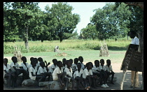 Sudan, Pacong, Children in outside class at village primary school with teacher standing beside blackboard in front of them.