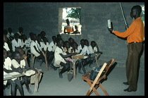 Sudan, Pacong, Dinka children at desks in primary school classroom with teacher standing at front.