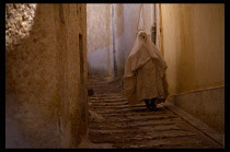 Algeria, Beni Izguen, Woman in white Muslim traditional clothing walking down steps.