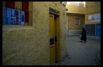 Egypt, Upper Egypt, Aswan, Elephantine Island colourful Nubian houses with woman in black walking past carrying bucket on her head.