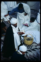 Ethiopia, Wolo Province, Lalibela, All night religious ceremony held on the night of a full moon.  Man in white turban and robe kneeling to read from book.
