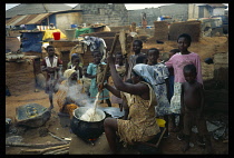 Ghana, Near Accra, Woman making the national dish of boiled and pounded yams known as fufu in a pot over a wood fire with children and villagers gathered around her looking on.