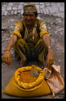Nepal, Kathmandu Valley, Patan, Man selling tumeric on roadside with hands and clothing stained yellow from the spice powder.