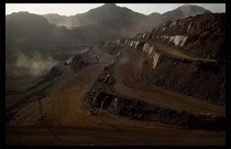 Mauritania, Industry, Mining, Iron mine  terraced slope distant machinery and drifting dust clouds.