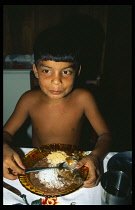 Brazil, Para, Portel, Pacaja River.  Young boy eating meal of manioc flour  farofa with onion   fried pescada  beans and rice  the staple diet.