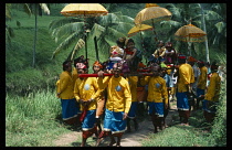 Indonesia, Bali, Ubud, Cremation procession with grandchildren of prince fetching holy water carried on litter with decorated golden sun shades accompanied by gamelan musicians.