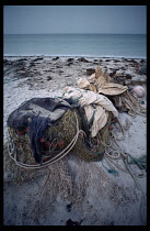 Mauritania, Fishing, Tangled pile of fishing nets  rope and anchor lying on sandy beach with sea beyond.