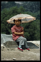 China, Beijing, Portrait of young girl seated on rock holding sun parasol.