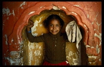 India, Madhya Pradesh, Children, Young girl playing in niche in museum wall with chipped and cracked red and ochre paintwork and scalloped edge.