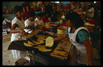 Mexico, Mexico City, Indoor market stall cooking and serving tortillas to customers eating at front.