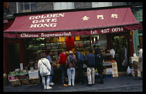 England, London, Chinatown, Shoppers outside Chinese supermarket looking at display of fruit and vegetables.