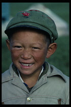 China, Xinjiang, Head and shoulders portrait of gap-toothed young boy wearing green army cap with red Communist star.