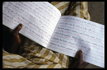 Ghana, Chereponi, Cropped view of man in adult literacy class with open exercise book on his lap.