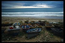 Morocco, Taghzout, Painted fishing boats pulled up onto rocky shore with sea and breaking surf beyond.