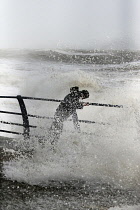 England, East Sussex, Hastings, Man braving the wild waves battering the promenade during storm.