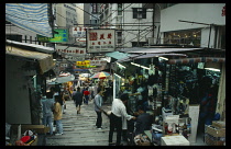 Hong Kong, Markets, Sloping  paved street lined with shops and stalls. People browsing with hanging advertising signs in English and Chinese overhead.