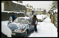 Weather, Snow, People scraping snow from car in residential street during winter.