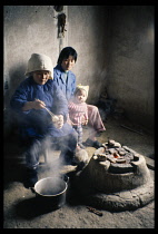 China,  Guizhou, Old woman serving boiled eggs to younger woman and little girl in farmhouse kitchen.