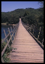 CHINA, Guangxi, Rongshui, Wooden footbridge crossing river with pedestrians and cyclist crossing at the far end.