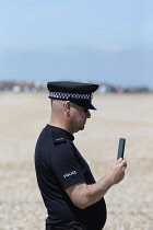 England, Kent, Dungeness, Police officer using his phone to video a beach landing of refugeees.